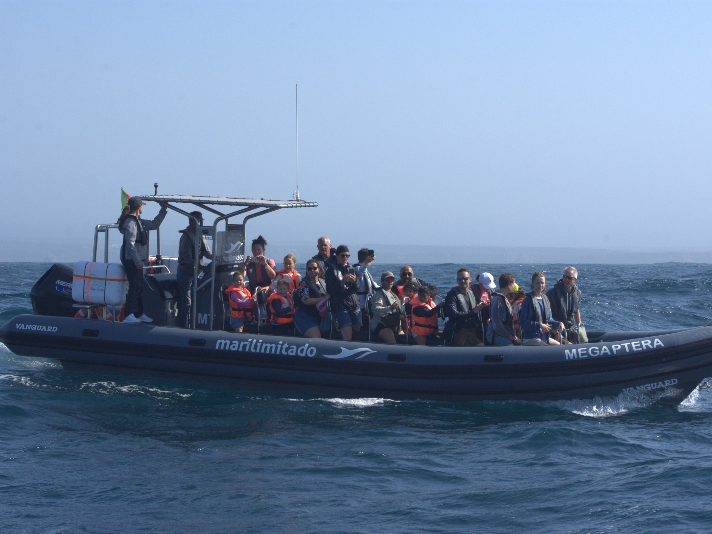 Boat with people wearing life jackets on a calm sea under clear blue skies.