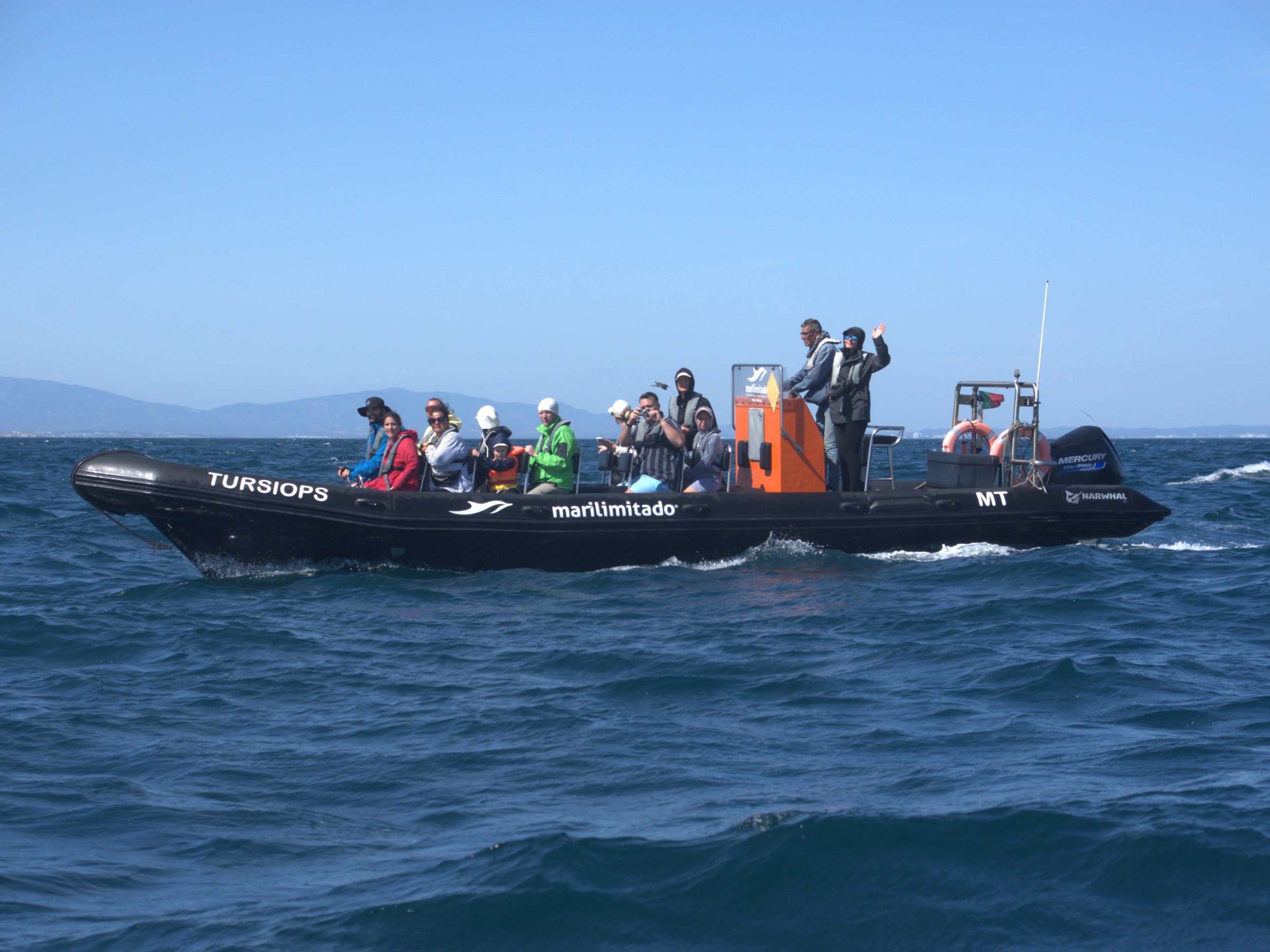 A group of people on a black boat with 'Tursiops' written on the side, navigating through the ocean.