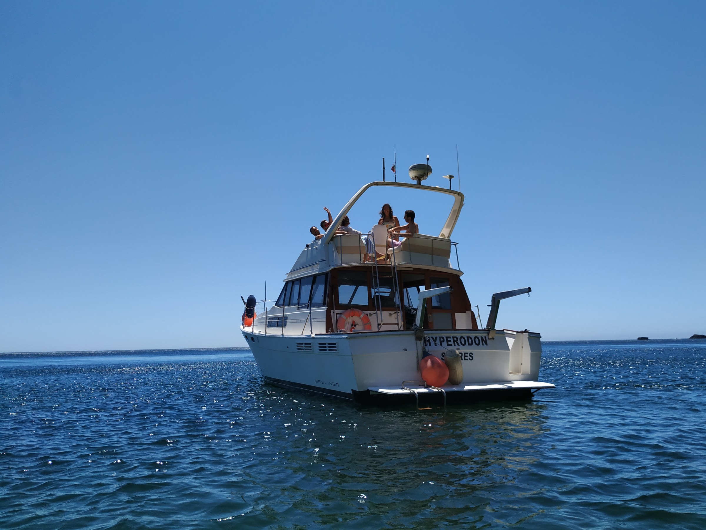 Boat with people on deck, floating in calm blue waters under clear sky.
